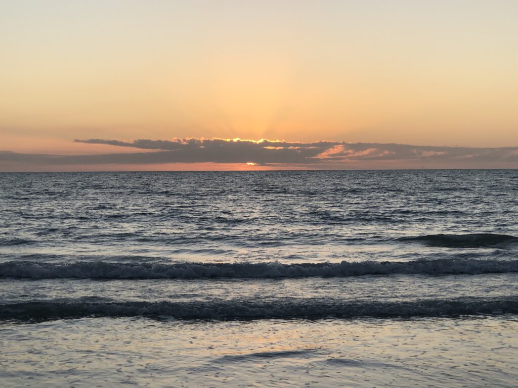 Image a sunset behinds the clouds and over the water in Madeira Beach, Florida